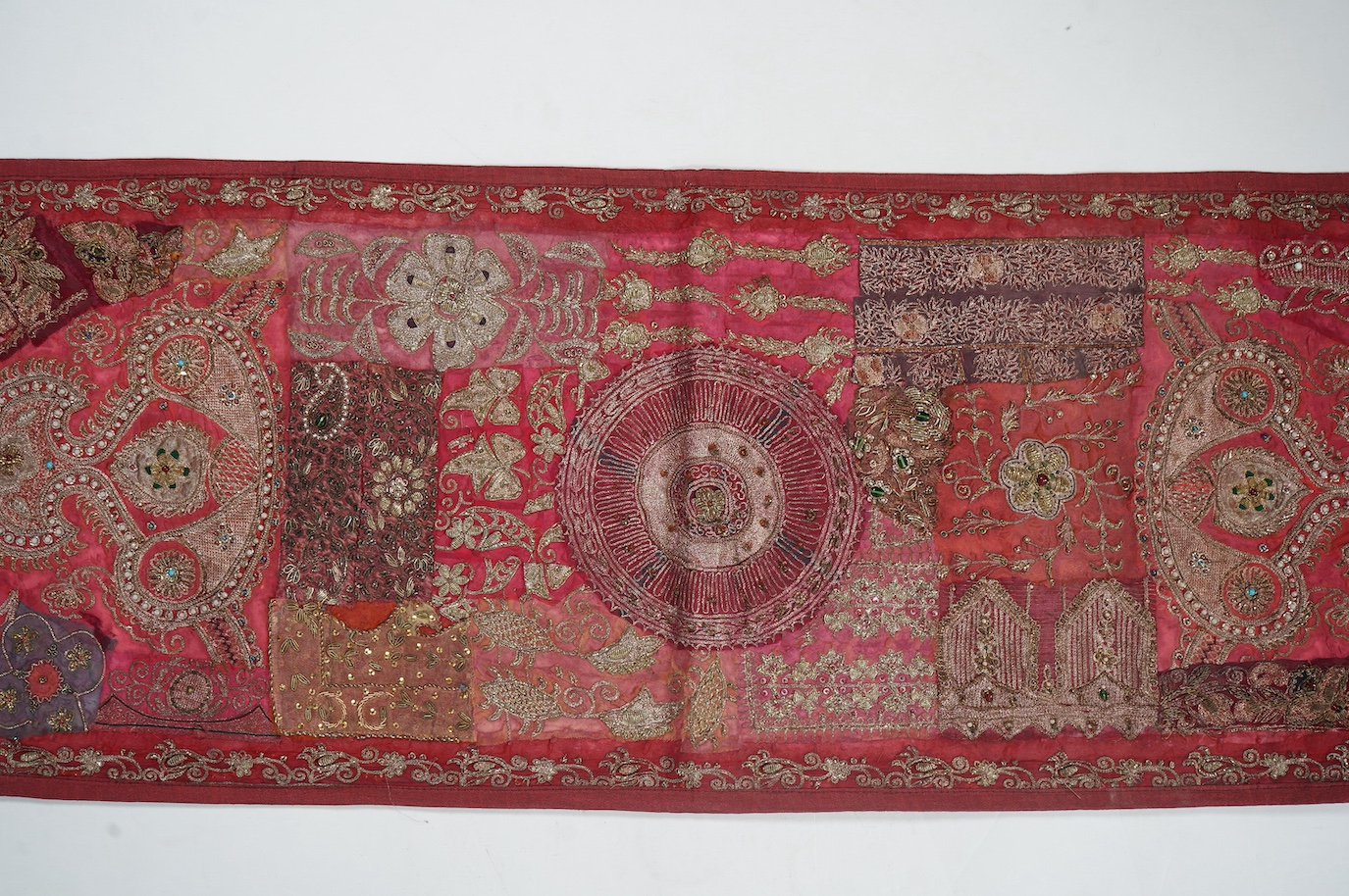 An Indian 20th century red silk marriage banner/hanging, ornately embroidered in silver and gold thread, with raised stump work flowers, corded and designed using simulated pearls and coloured beads etc., 74cm x 43cm. Co